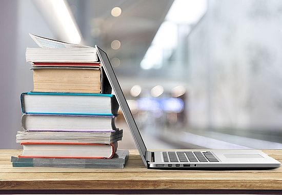 Laptop aufgeklappt, an Bücherstapel gelehnt