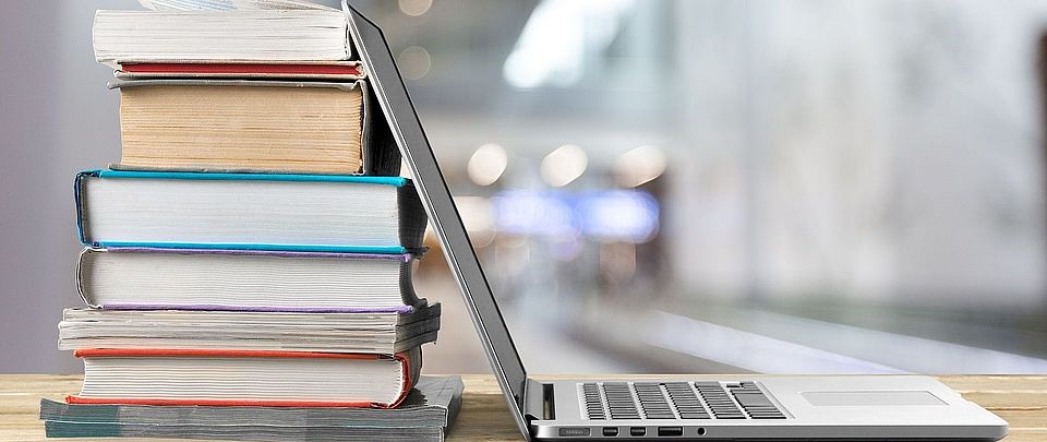 Laptop, aufgeklappt, an Bücherstapel gelehnt