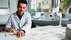 Projektmitarbeiter Gabriel Schaffter reinigt die Zettel einzeln mit einem Schwamm und einem Absauggebläse.