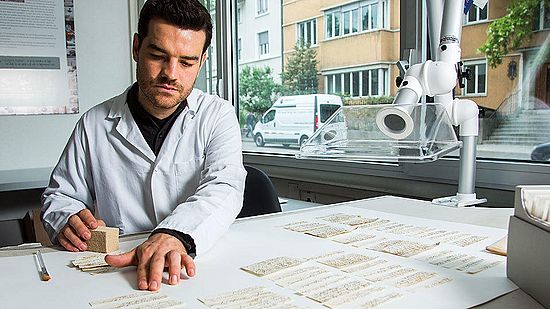 Projektmitarbeiter Gabriel Schaffter reinigt die Zettel einzeln mit einem Schwamm und einem Absauggebläse.