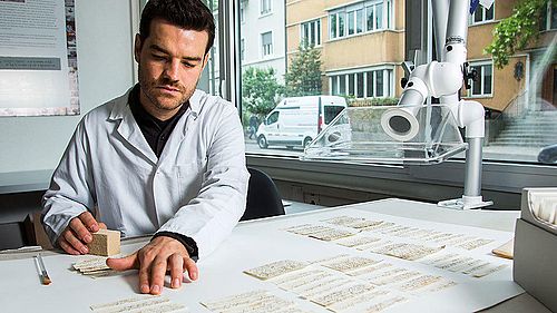 Projektmitarbeiter Gabriel Schaffter reinigt die Zettel einzeln mit einem Schwamm und einem Absauggebläse.